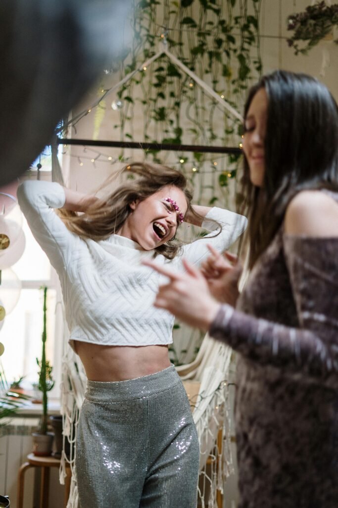 Two women dancing and laughing at an indoor celebration.